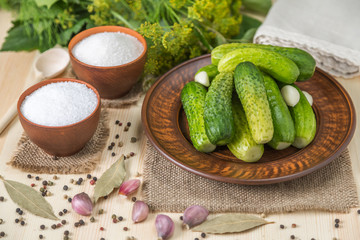 Salted cucumbers in a bowl and ingredients on the table from pine boards.