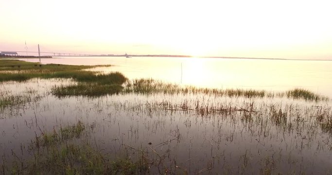 Flying over marsh grass in Charleston harbor at sunrise with a leisure boat cruising in the water.
