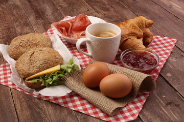 breakfast on table with bread rolls, croissants, coffe and eggs