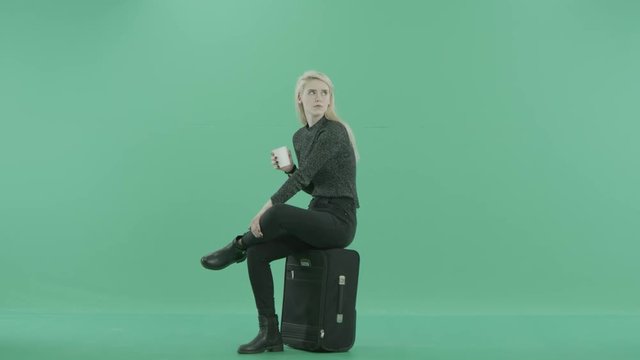 a woman drinks coffee sitting on the luggage