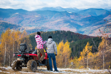 Rear view of girl standing on a red quad bike and keeps the shoulder standing next guy enjoying the mountain autumn landscape © anatoliy_gleb