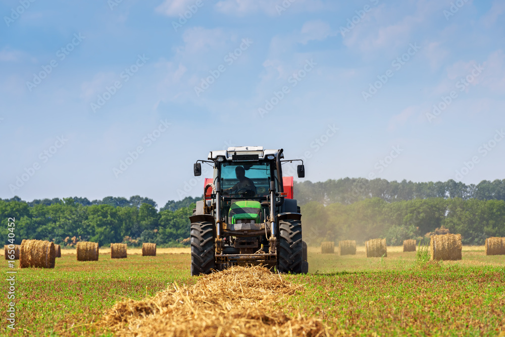 Poster tractor in a farmer field with balls of straw.