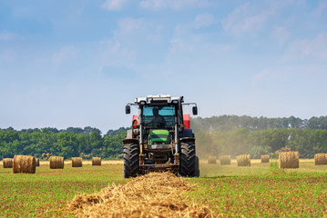 Obraz premium Tractor in a farmer field with balls of straw.