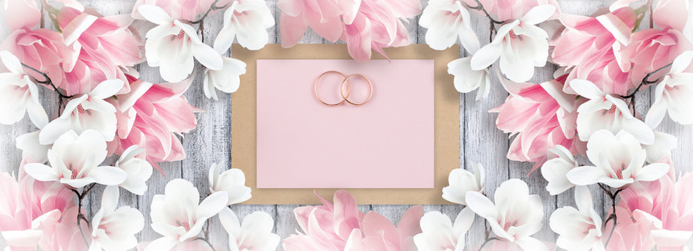 Magnolia and bridal rings with paper greeting card for wedding on background of shabby wooden planks