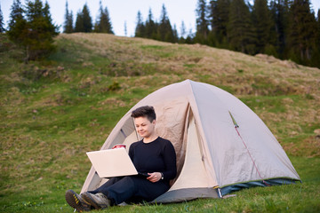 Happy young female sitting in her tent in the mountains and working on a laptop copyspace technology connectivity mobility wireless connection project