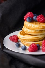 Stack of gluten free pancakes with raspberries and blueberries on white plate and black background