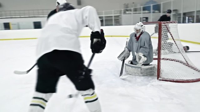 Tracking of ice hockey player practicing in rink: forward in white gear training shooting puck and trying to score goal as goaltender blocking net