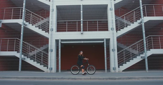 CINEMAGRAPH - seamless loop. Young stylish Caucasian female riding her bicycle, urban background. 4K UHD RAW edited footage