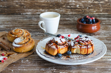 Fresh Delicious  cinnamon fruit rolls with powdered sugar and caramel, ceramic bowl with blueberies and grains of pomegranate on the back. Sweet food backround.