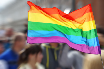 Waving gay flag and crowd of people on background. Concept of LGBT rights and parade