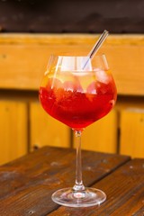 glass of sparkling refreshing long drink in balloon glass decorated by slices of orange. Glass is set on wooden table in porch of mountain restaurant and reflect surrounding treeline.