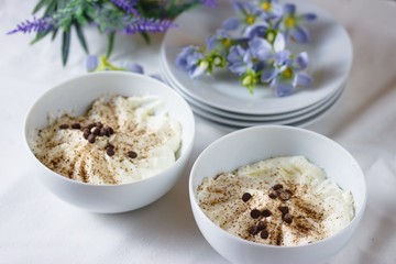 Two white china bowls of sour cream mousse dessert sprinkled with chocolate and chocolate chips