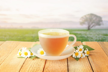 Hot chamomile tea in cup with flowers on wooden table outdoor