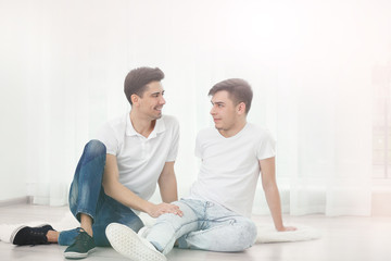 Fototapeta na wymiar Happy gay couple sitting on floor against window