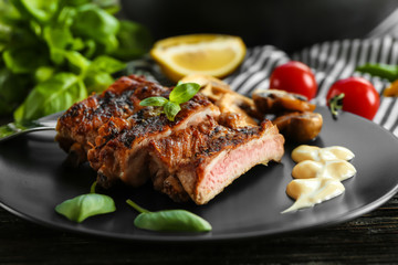 Black plate with delicious grilled sliced spare ribs with garnish on wooden table