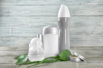 Different deodorants and leaves on wooden background
