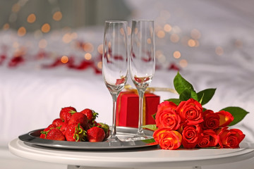 Romantic composition with strawberry and red roses on table in bedroom. Honeymoon concept