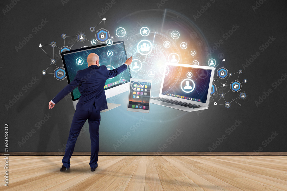 Poster businessman in front of a wall with computer and devices displayed on a futuristic interface with bu