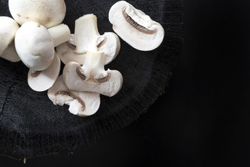 White mushrooms champignons whole and sliced on black wooden background