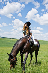 Young pretty girl riding a horse on a field at sunny day.