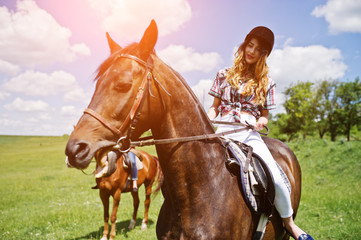 Obraz premium Tow young pretty girls riding a horses on a field at sunny day
