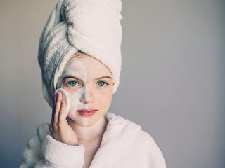 Funny little girl with a mask for skin face and with a towel on her head, portrait on a gray background