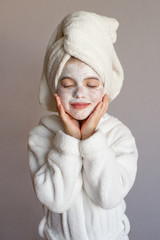 Funny little girl with a mask for skin face and with a towel on her head, portrait on a gray background © polya_olya