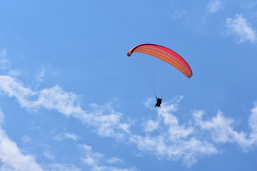 Red tandem paraglider in blue sky with fluffy white clouds