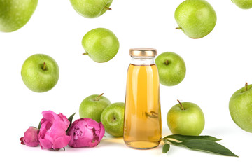 Apple golden juice in bottle. Fruit soft drink in a glass bottles isolated on white background. Pink flowers peonies and flying apples
