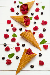 Sweet fresh organic raspberries in waffle cones. Fresh berries in cones on white wooden background with blank space. Summer and healthy food concept