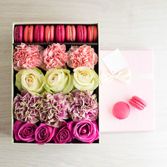 pink gift box with pink and beige roses, chrysanthemums and French sweet macaroons on light wooden background. For the celebration of different holidays
