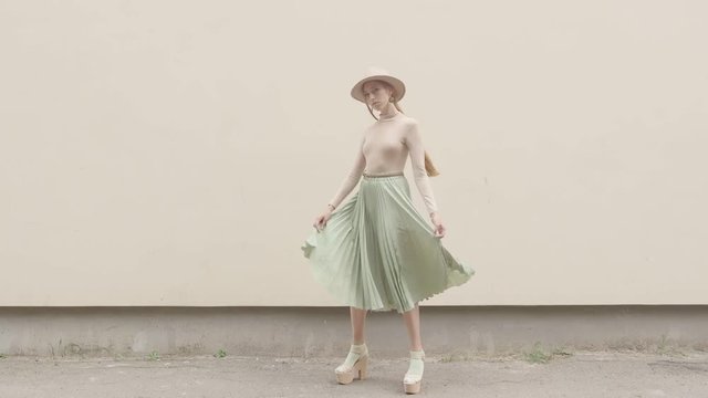 Model in a hat and a long skirt walks on the camera against the wall