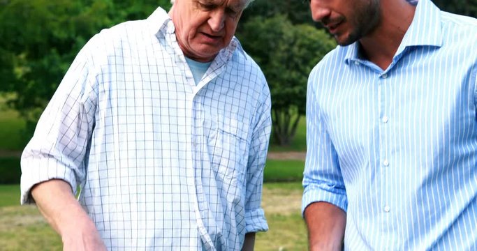 Father and son preparing food on barbecue and interacting with each other in park
