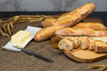 still life with French fresh bread baguettes with poolish on wooden a cutting board, wheat and butter, shallow dof