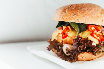 Delicious and appetizing burger with chicken cutlet, basil and chili pepper on a white wooden background