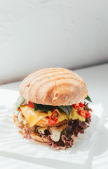 Delicious and appetizing burger with chicken cutlet, basil and chili pepper on a white wooden background