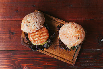 A real burger on a wooden background. With a large and juicy cutlet tender cheese sauce and mustard. Rustic