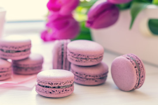 Violet sweet delicious macaroons and fresh tulips on white background. Cup of hot tea. Shallow depth of field. Coloring toned photo.