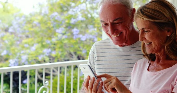 Happy senior couple using mobile phone in balcony
