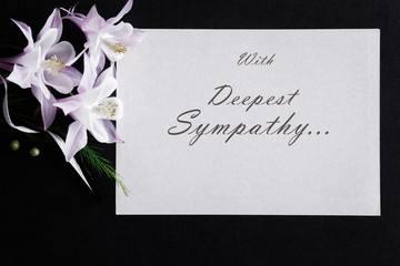 White condolence card with text and fresh flowers on the dark background.