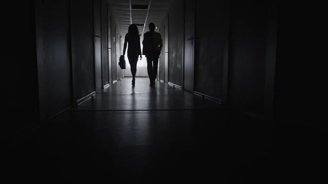 PAN with low angle of businesswoman with briefcase and businessman walking along dark corridor in slow motion