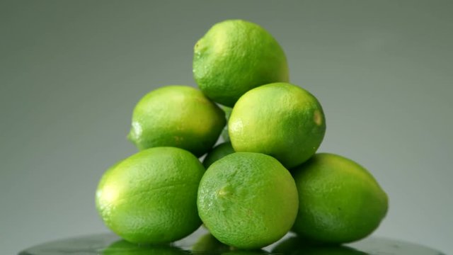 Heap of fresh limes rotating on reflective surface