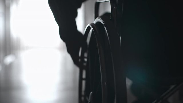 Tracking with close up of male hand turning wheels of manual wheelchair 
