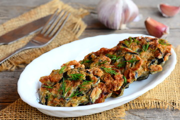 Crispy fried eggplant cutlets with garlic and dill on a white plate and a burlap textile. Fork and knife on a vintage wooden background. Gluten-free fried eggplant cutlets recipe. Closeup