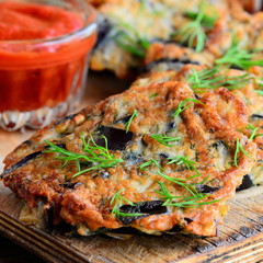 Simple fried eggplant cutlets with garlic and dill on a white plate and a vintage wooden table. Tomato ketchup sauce in a glass bowl. Veggie eggplant cutlets idea. Closeup