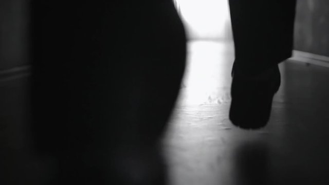 Tracking with low-section of silhouette of legs of man walking along corridor; black and white slow motion shot