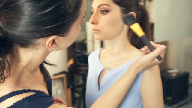 Young beautiful woman applying make-up by make-up artist