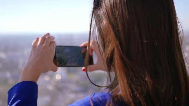 Beautiful young girl is taking pictures on the phone of a panorama of the city from a height. SLOW MOTION. HD, 1920x1080.
