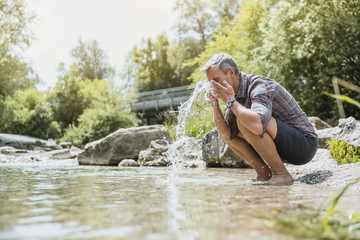 Hiker having a break at the riverbank washing his face