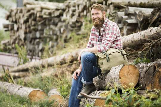Laughing bearded man sitting on stack of wood